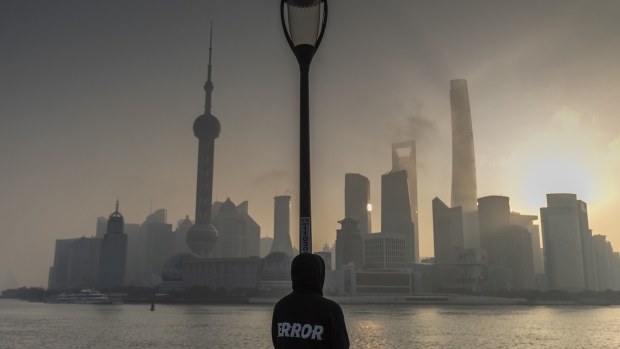 A pedestrian stands along the Bund in front of buildings in the Lujiazui Financial District at sunrise in Shanghai, China, on Tuesday, Jan. 4, 2022. A wall of maturing debt and a surge in seasonal demand for cash will test China’s financial markets this month, putting pressure on the central bank to ensure sufficient liquidity. Photographer: Qilai Shen/Bloomberg